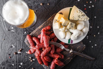 cheese pieces on a plate, Mini Sausages, Smoked Salami Sticks, wooden cutting board, glasses with...