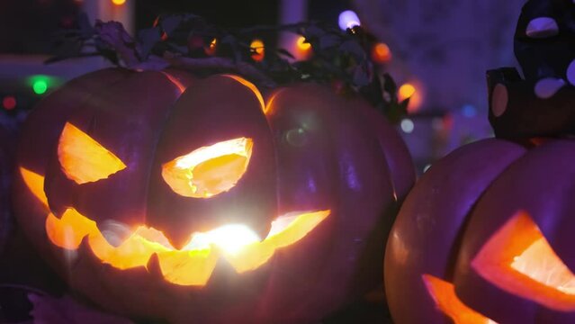 Close up carved pumpkins of different sizes with flickering light inside in fog background of colorful garlands. tracking shot. Festival holiday background Halloween time.