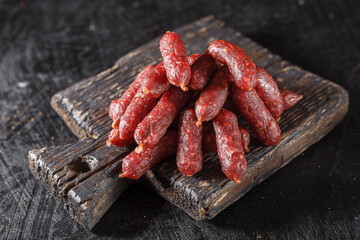 Mini Sausages, Smoked Salami Sticks, old wooden cutting board, on a black isolated background