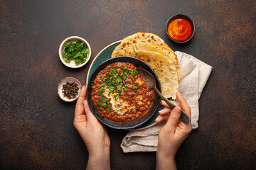 Female hands holding a bowl and eating traditional Indian Punjabi dish Dal makhani with lentils and...