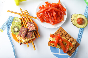 glass of milk, crackers and fruits, avocado and meat snacks on a plate, dried pieces of Carpaccio, dumbbell and sports ruler, on a white isolated background