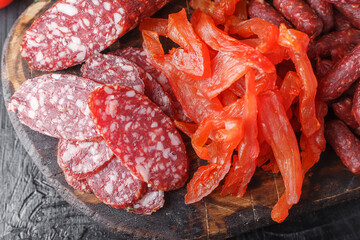 fresh herbs and vegetables, dry-cured sausage, dried pieces of Carpaccio meat, small salami sticks, vintage wooden cutting board, on a black isolated background