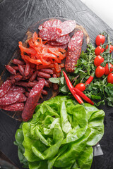fresh herbs and vegetables, dry-cured sausage, dried pieces of Carpaccio meat, small salami sticks, vintage wooden cutting board, on a black isolated background
