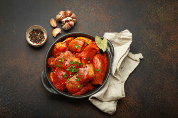 Raw uncooked chopped pieces of meat marinated with seasonings and parsley in black casserole dish...