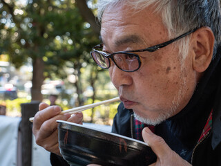 An older Japanese man eating with chopsticks - 653952117