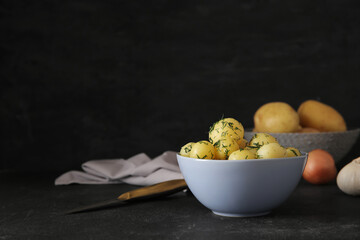 Bowl with boiled baby potatoes on black background