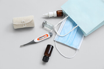 Shopping bag with medical mask, elastic bandage and thermometer on grey background
