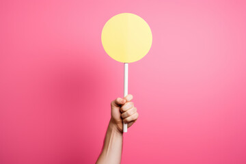 Hand holding yellow sign mockup against pink background. This image can be used for candy-themed designs or to represent sweetness and joy.