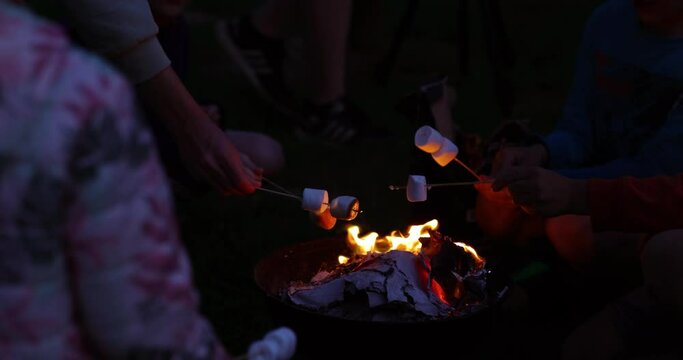 View of children roasting marshmallows on skewers over fire pit at campsite. Family vacation.