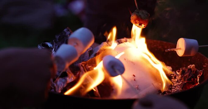 View of children roasting marshmallows on skewers over fire pit at campsite. Family vacation.