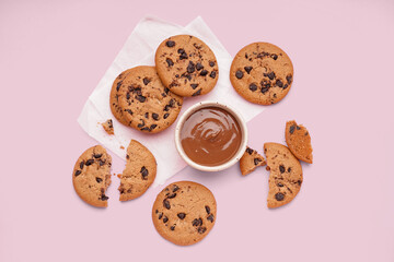 Tasty cookies with chocolate chips and bowl of sauce on pink background