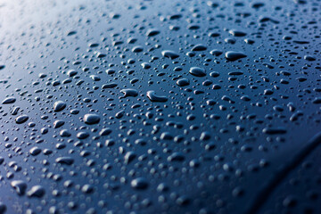 Abstract rain or water drops different size on a blue car hood surface with shiny reflections....
