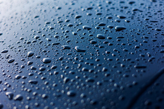 Abstract rain or water drops different size on a blue car hood surface with shiny reflections. Water droplets on dark iron surface and texture. Background and water texture for design.