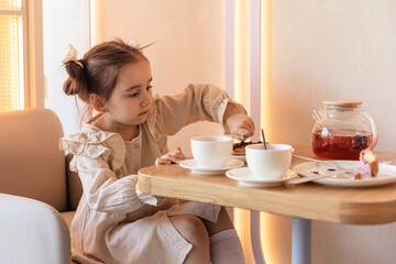 Cute little brunette girl drinking a tea with spoon at the table and eating some cookies. Family...