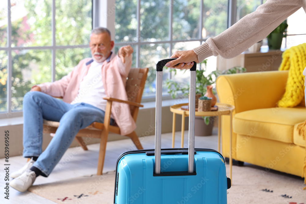 Wall mural Mature woman with suitcase leaving her husband at home, closeup. Divorce concept