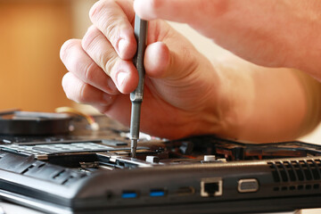 Repaiman with screwdriver fixing disassembled laptop parts. Technical support and fixing gadgets problems. Servicing, repairing, cleaning, maintaining computers. Repair shop. Hardware maintenanc