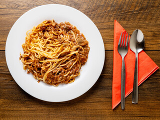 Portion of high quality spaghetti Bolognese on white plate and wooden table. Premium quality dish made with fine products.