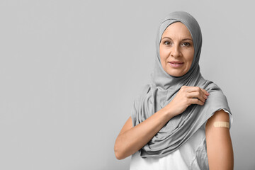 Mature Muslim woman with medical patch on arm against grey background. Vaccination concept
