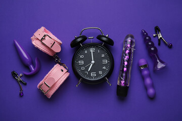 Alarm clock with sex toys on violet background