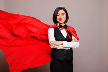 Smiling confident asian receptionist standing in fluttering superwoman red cape and looking at...