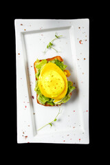 Egg benedict on a white plate on a black background