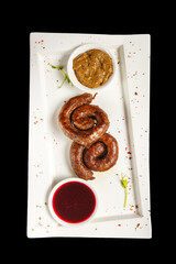 Grilled sausages with sauce on a white plate isolated on black background