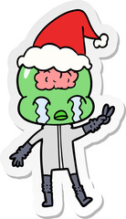 hand drawn sticker cartoon of a big brain alien crying and giving peace sign wearing santa hat