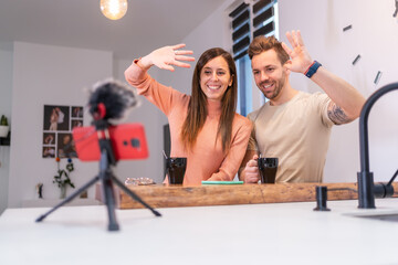 Young couple waving while vlogging at home