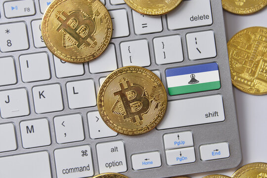 national flag of lesotho on the keyboard with bitcoin coins on a grey background.