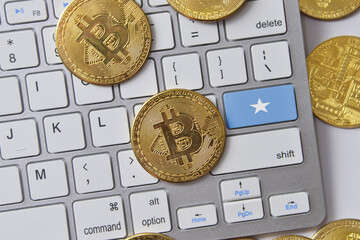 national flag of somalia on the keyboard with bitcoin coins on a grey background.