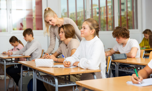Group of diligent school kids and teacher during lesson in classroom in secondary school