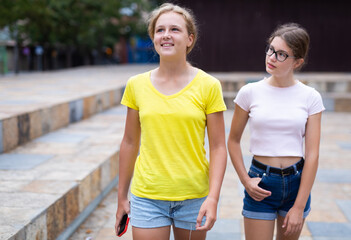 Two teenager girls walking together through park in afternoon.