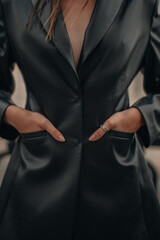 Fashion details of a black leather jacket with pocket and silver ring accessories. Fancy outfit, female accessories