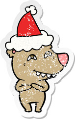 hand drawn distressed sticker cartoon of a bear showing teeth wearing santa hat