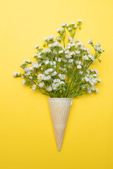 bouquet of wildflowers daisies in an ice cream cone on a yellow background.Flat top view.