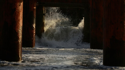 Close up of old wooden columns supporting pier in sea. Creative. Strong waves and white sea foam. - Powered by Adobe