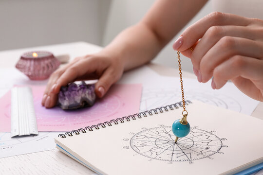 Astrologer using zodiac wheel and pendulum for fate forecast at table, closeup. Fortune telling