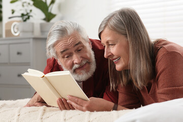 Lovely senior couple reading book on bed at home