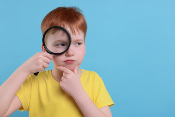Thoughtful boy looking through magnifier glass on light blue background, space for text