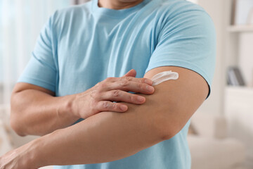 Man applying body cream onto his arm indoors, closeup