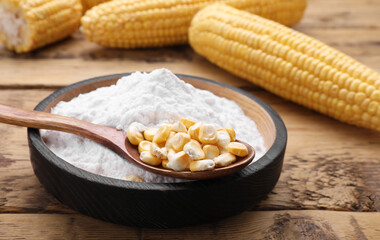 Bowl of corn starch and kernels on wooden table, closeup