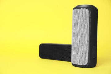 Portable bluetooth speakers on yellow background, space for text. Audio equipment