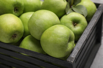 Fresh green apples in black crate on table, closeup
