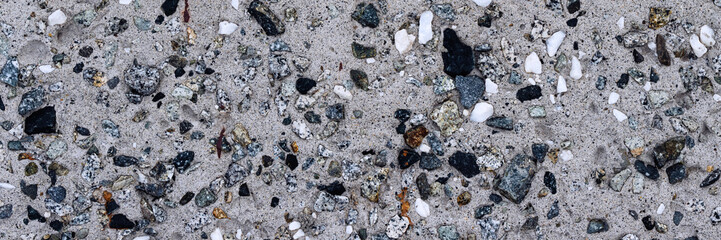 Concrete wall texture with pebbles. Decorative rough concrete surface with white, black and gray stones. Wide panoramic texture for background and design.