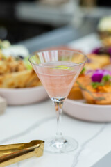 pink cosmopolitan cocktail sitting on bar in restaurant with platters of appetizers in the background 