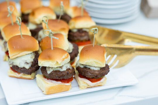 platter of mini cheeseburger sliders on plate with gold serving utensil at happy hour function