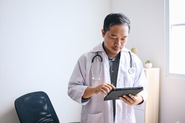 Serious Asian doctor working with digital tablet computer in modern office at hospital, tele...