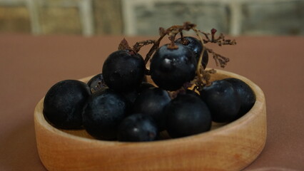 a bunch of black grapes in a round wooden container. light brown background