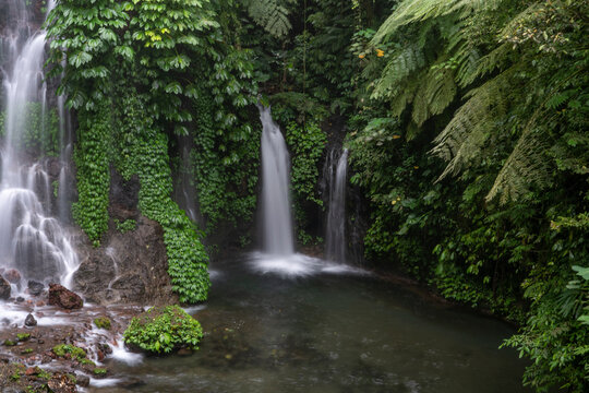 A beautiful waterfall in the jungle of Southeast Asia. A stream of water falls from high rocks between the vegetation, breaking into two streams, creating fog. High humidity in the jungle.