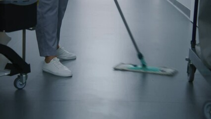 Close up of health worker mops floor in medical facility hallway. Mature nurse or female cleaner takes care of cleanliness in hospital corridor. Professional medical personnel work in modern clinic.